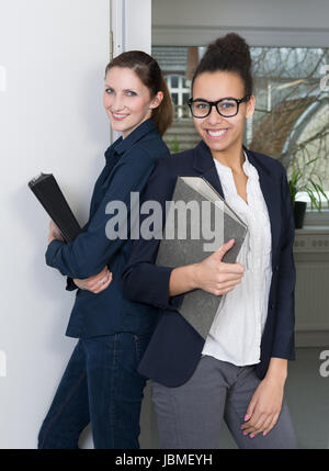 Zwei junge Büroangestellte nebeneinander stehen und halten Akten in ihren Händen. Foto Stock