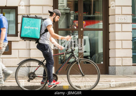 Un ciclista Deliveroo di prelevare il suo lavoro successivo sul suo telefono cellulare nella zona centrale di Londra, Regno Unito Foto Stock