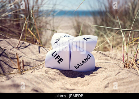 Origami fortune teller in vacanza in spiaggia per il concetto di equilibrio tra lavoro e vita familiare scelte Foto Stock