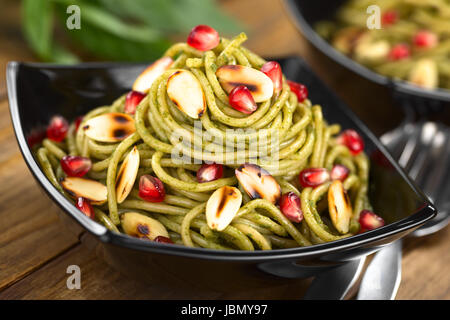 Pasta al pesto fatta di basilico e spinaci guarnito con mandorle tostate e melograno servito in tazza nera (messa a fuoco selettiva, Focus su la mandorla e melograno appena sotto la parte superiore del piatto) Foto Stock