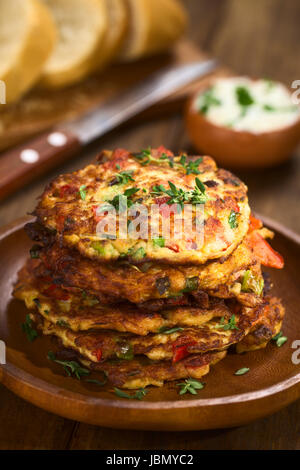 Verdure e uova frittella fatta di zucchine, il peperone rosso, uova, i cipollotti e il timo impilate su di un piatto di legno con baguette fette e yogurt dip in retro (messa a fuoco selettiva, messa a fuoco sulla parte anteriore del rametto di timo sulla parte superiore delle frittelle) Foto Stock