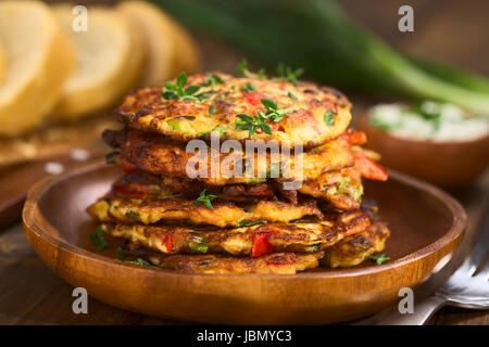 Verdure e uova frittella fatta di zucchine, il peperone rosso, uova, i cipollotti e il timo impilate su di un piatto di legno con baguette fette e yogurt dip in retro (messa a fuoco selettiva, messa a fuoco sulla parte anteriore del rametto di timo sulla parte superiore delle frittelle e sulla parte anteriore del top frittelle) Foto Stock