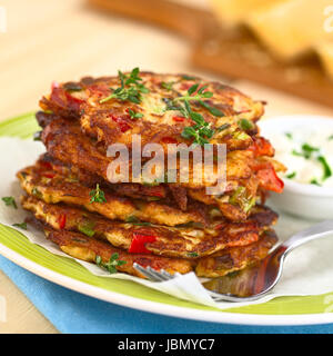 Verdure e uova frittella fatta di zucchine, il peperone rosso, uova, i cipollotti e il timo impilati su una piastra con forcella e yogurt dip sul lato (messa a fuoco selettiva, messa a fuoco sulla parte anteriore del rametto di timo sulla parte superiore delle frittelle e sulla parte anteriore del top frittelle) Foto Stock