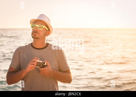 Ritratto di giovane turista guy holding fotocamera retrò al mare pronto a scattare foto. Vacanze estive e i concetti di viaggio. Copia dello spazio. Foto Stock