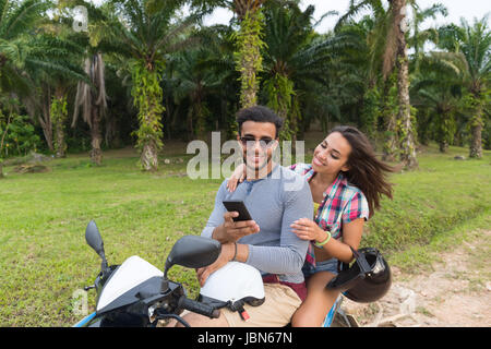 Matura in sella moto, giovane uomo e donna utilizzando una cella Smart Phone viaggiare in bicicletta sulla foresta tropicale Road Foto Stock