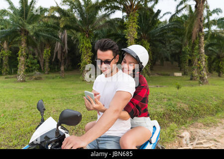 Matura in sella moto, giovane uomo e donna utilizzando una cella Smart Phone viaggiare in bicicletta sulla foresta tropicale Road Foto Stock