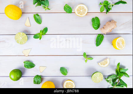 Pattern colorati di menta, calce, limone,fettine di zenzero. . Cedri e limoni tagliati a fette e intera con foglie. Bianco su sfondo di legno. Spazio libero per il testo Foto Stock
