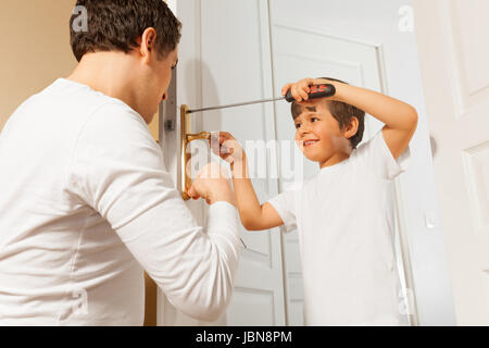Ritratto di sei anni vecchio ragazzo montaggio maniglia della porta servendosi di un cacciavite sotto la supervisione del padre Foto Stock