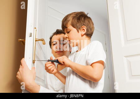 Ritratto di giovane padre aiutando i suoi sei anni vecchio figlio di fissare dei comandi di apertura delle porte con un cacciavite Foto Stock
