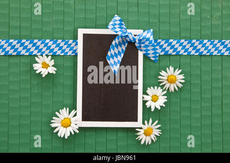 Kleine Tafel auf Gruen mit Margeriten und blau-weissem Geschenkband Foto Stock