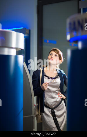 Piuttosto, giovane donna il ritiro di denaro dalla sua carta di credito presso uno sportello ATM (SHALLOW DOF; dai toni di colore immagine) Foto Stock