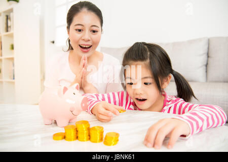 Madre figlia di insegnamento mettendo monete nel salvadanaio. Bilancio familiare e risparmio concetto per il futuro nel salotto di casa. attività della famiglia C Foto Stock