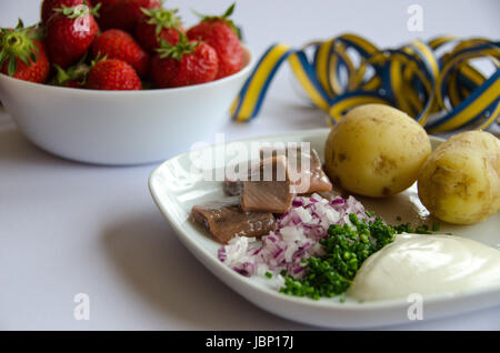 Aringhe in salamoia con patate di primizia, erba cipollina, cipolla rossa e sourcream su una piastra di porcellana. Una tazza di fragole sul lato. Foto Stock