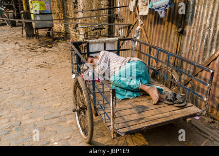 Un uomo dorme sul suo risciò ciclo su una strada nel quartiere nuovo mercato Foto Stock