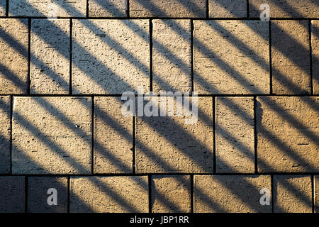 Pietre per pavimentazione in calcestruzzo posato sul terreno illuminato dal sole e con ringhiera in linee di ombra in corrispondenza di un angolo Foto Stock