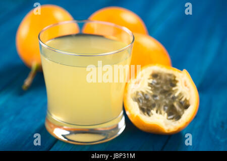 Succo di frutta fresco fatto di dolci granadilla o grenadia (lat. Passiflora ligularis) in vetro con una mezza granadilla accanto ad essa (messa a fuoco selettiva, messa a fuoco sul bordo anteriore del vetro) Foto Stock