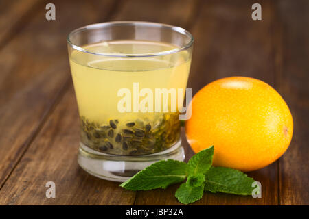 Succo di frutta fresco fatto di dolci granadilla o grenadia (lat. Passiflora ligularis) con i suoi semi in vetro, granadilla frutta e foglia di menta sul lato (messa a fuoco selettiva, messa a fuoco sul bordo anteriore del vetro) Foto Stock