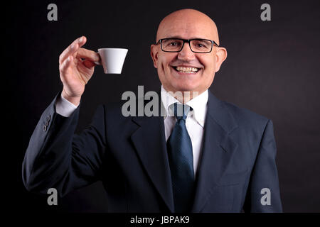 Bald vecchio sorridente imprenditore tenendo una tazza di caffè espresso italiano Foto Stock