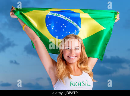 Felice fan del calcio brasiliano squadra, allegro Pretty girl su stadium il tifo nel supporto, mantenendo la grande bandiera nazionale del Brasile, le persone attive che viaggiano a Coppa del Mondo Foto Stock