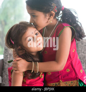 Indian ragazza baciare la sua sorella più giovane con l'amore. Famiglia asiatica a casa. Belle figlie in India tradizionale sari. Foto Stock