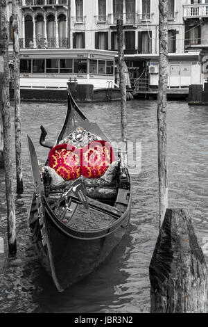 Gondola- una gondola solitario siede ormeggiate lungo il Canal Grande a Venezia. Ero affascinato dal suo colore rosso brillante sedile ammortizzato per i suoi passeggeri. Foto Stock