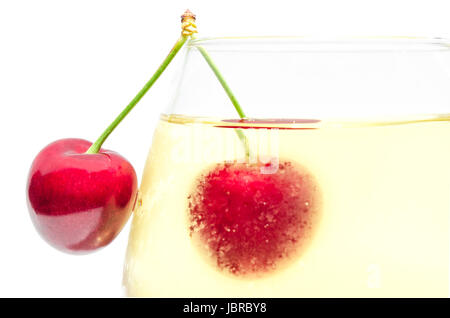 Coppia di ciliegia matura bacche sul bordo superiore della piena colmi wineglass con fredda Vino bianco isolato di close-up Foto Stock