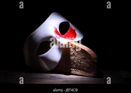 Impero romano concetto. Maschera bianca con macchia rossa giacente sul pane su sfondo nero Foto Stock