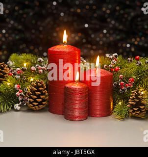 Tre candele rosse con albero di Natale rami e pigne decorate Foto Stock