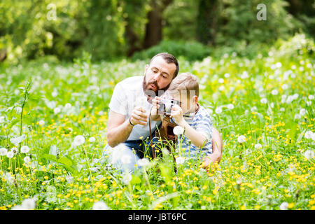 Giovane padre con piccolo ragazzo con telecamera in estate park. Foto Stock