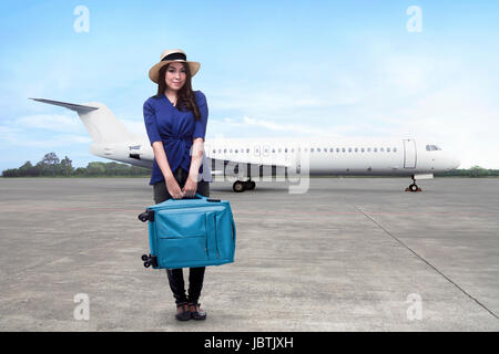 Felice donna asiatica passeggero che indossa hat holding valigia in attesa aereo a decollo Foto Stock