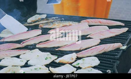 Lo chef fatiche sopra una griglia aperta la frittura di pesce, rapans e calamari. La cottura di filetti di sgombro al grill per pesci di frumento. In terra di barbecue con pesce grillin Foto Stock