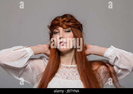 Junge Fraumädchen attraktive mit langen haaren roten ritratto im vor grauem Hintergrund Foto Stock