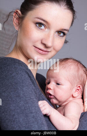 Glückliche junge Mutter hält ihr neugeborenes tipo vor der Brust und lächelt Foto Stock