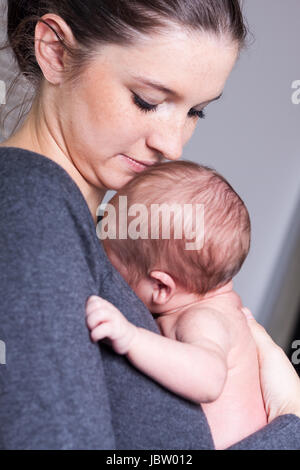 Glückliche junge Mutter hält ihr neugeborenes tipo vor der Brust und lächelt Foto Stock