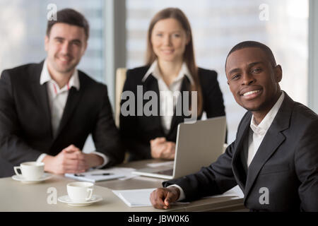 Attraente afro american allegro imprenditore guardando la telecamera seduto alla scrivania, giovane africana manager incontro di leader per i subordinati a sfondo, Foto Stock