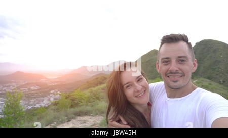 Coppia sorridente tenendo selfie in montagna, antenna. vista città Foto Stock