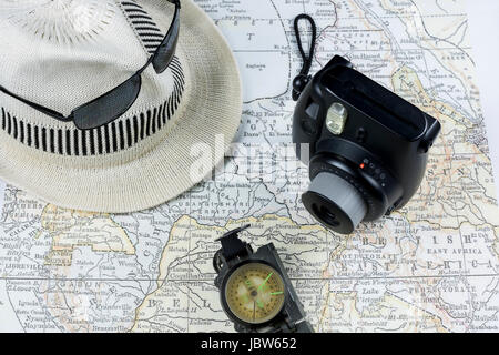 Macchina fotografica d'epoca, occhiali da sole, bussola, cappello bianco su un'antica mappa, che illustra l'emozione e la pianificazione necessari per esplorare una nuova destinazione Foto Stock