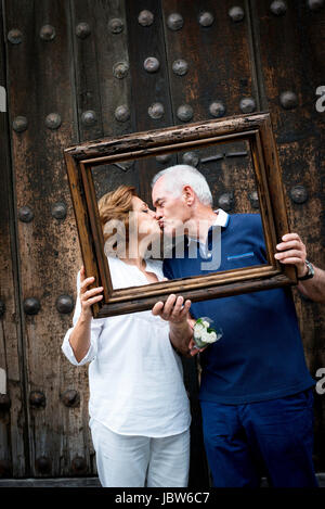 Ritratto di Coppia senior, baciare, tenendo il telaio in legno nella parte anteriore delle loro facce, Città del Messico, Messico Foto Stock