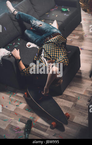 Ubriaco barbuto giovane uomo che dorme sul divano in camera disordinato after party Foto Stock