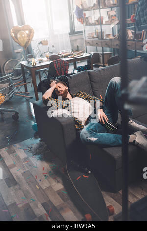 Ubriaco barbuto giovane uomo con bottiglia di dormire sul divano dopo essere partito Foto Stock