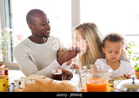 Giovani interracial famiglia con bambini piccoli aventi la prima colazione. Foto Stock