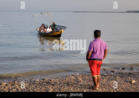 Bandar Abbas, Hormozgan Provincia, Iran - 16 aprile, 2017: Un uomo appare come una barca con una famiglia di iraniani a bordo, ormeggio a terra. Foto Stock