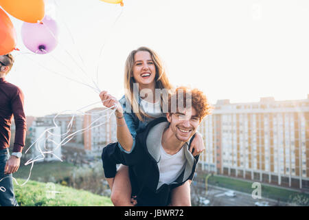 Amici godendo di parte del tetto, giovane dando giovane donna piggyback Foto Stock