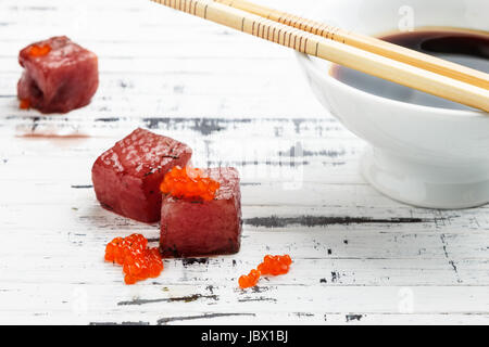 Tonno sashimi immerso in salsa di soia con uova di salmone sul vecchio legno bianco bordo con bacchette e ciotola con semi di soia. Pesce crudo in tradizionale stile Giapponese. Foto Stock