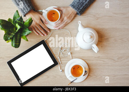 Ragazza seduta al tavolo e bevande di tè verde. Tablet con uno spazio vuoto e le cuffie si trova nelle vicinanze. Foto Stock