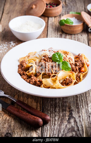 In casa tradizionale pasta italiana pappardelle bolognese servita con Grana Padano formaggio sulla tavola in legno rustico Foto Stock