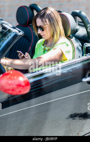 Giovane donna alla guida di una vettura cabriolet distratto con il suo telefono e risultare pericoloso per il traffico intorno a. Foto Stock