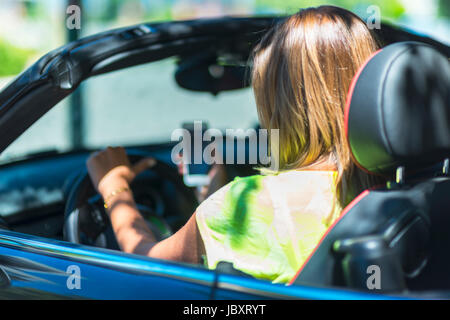 Giovane donna alla guida di una vettura cabriolet distratto con il suo telefono e risultare pericoloso per il traffico intorno a. Foto Stock