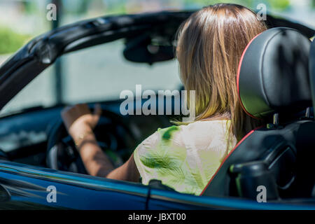 Vista dal retro di una giovane donna bionda alla guida di una cabriolet auto senza il tetto. Foto Stock