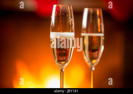 Immagine macro di due bicchieri riempiti con champagne frizzante con caminetto sullo sfondo Foto Stock